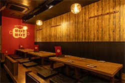肉バルダイニングMeat Meetの店内写真：木製で統一されている壁とテーブル、椅子の上に暖色のライトが吊り下がっていて、奥の方にはお店のロゴが白抜きされたえんじ色の暖簾がかかっている